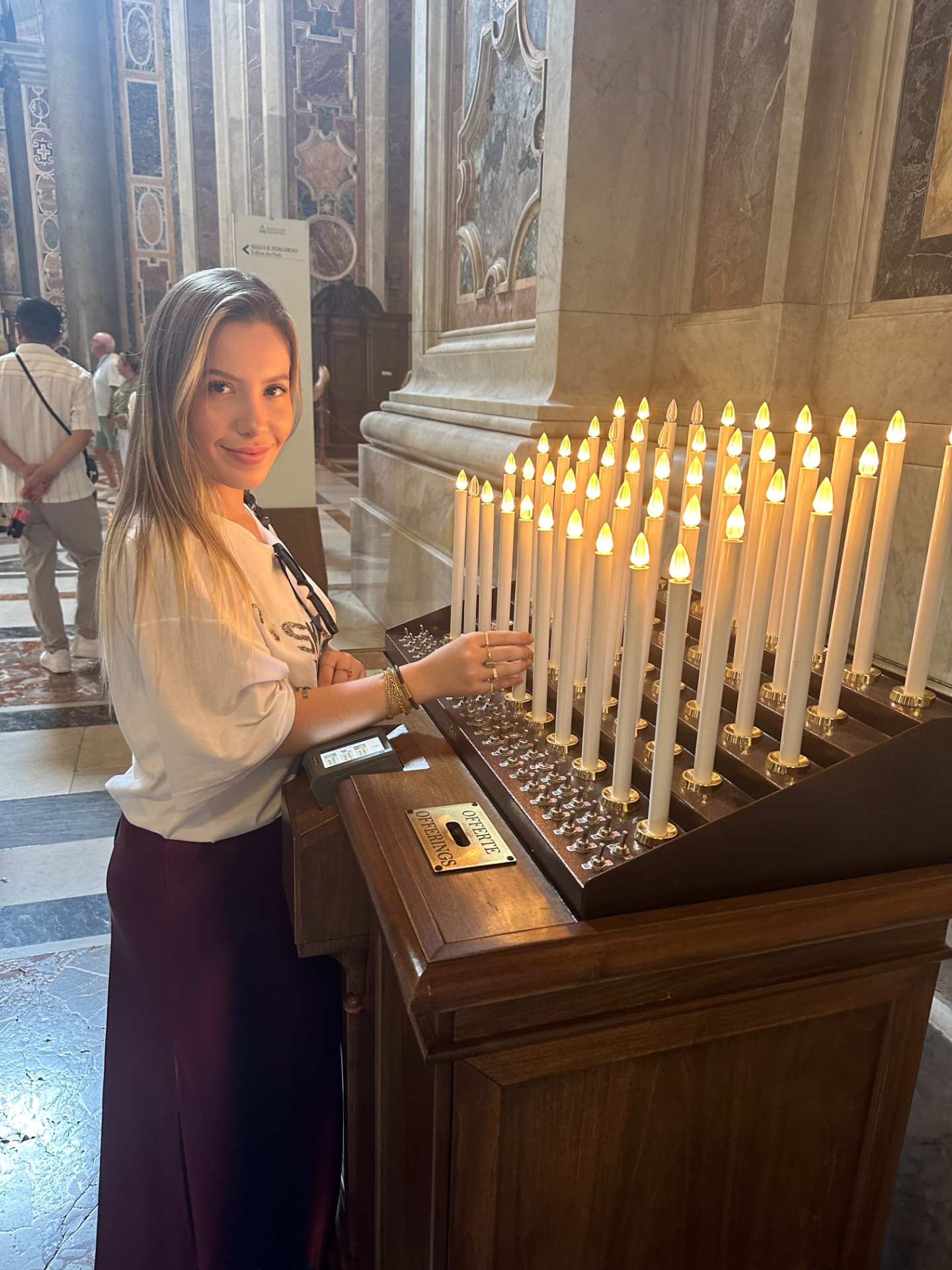 Yza sorrindo ao lado de velas acesas em suporte de madeira dentro de uma igreja histórica