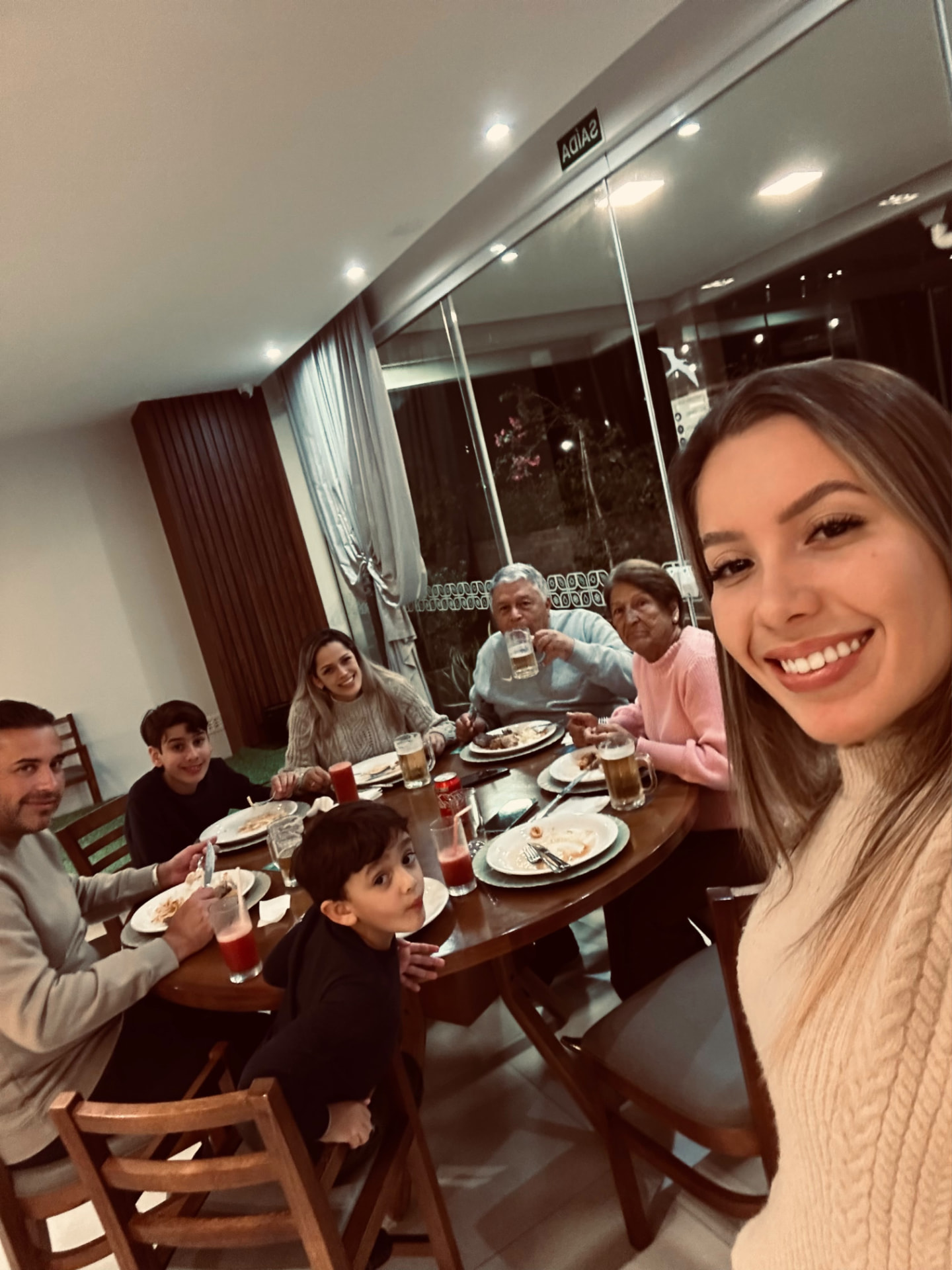 Yza tirando uma selfie enquanto a família se reúne ao redor da mesa de jantar